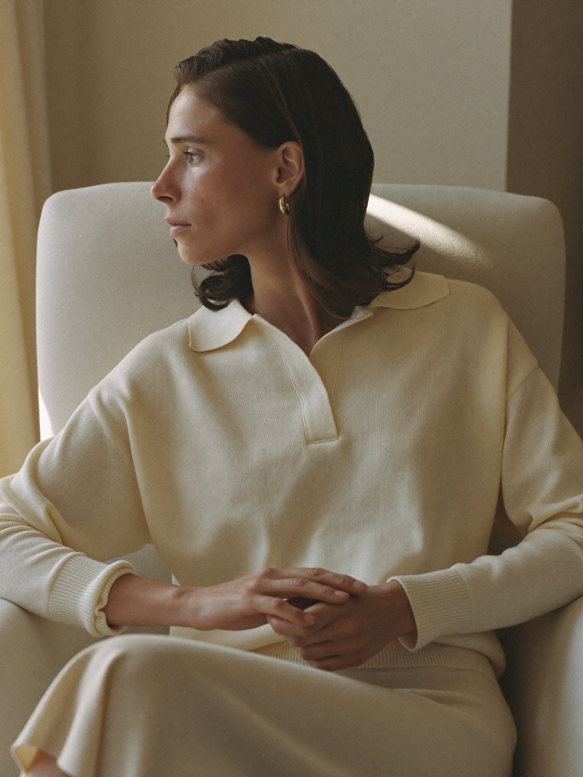 Fine-gauge cream knit polo in warm window light